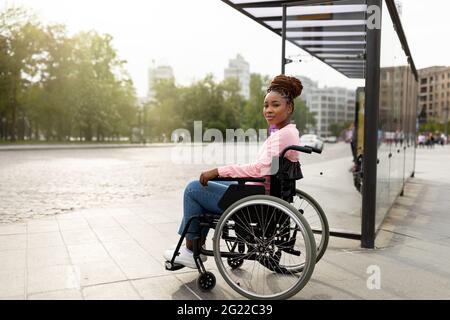 Une jeune femme noire handicapée en fauteuil roulant ne peut pas monter à bord d'un véhicule adapté aux personnes handicapées, attendant à l'arrêt d'autobus Banque D'Images