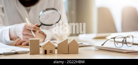 Recherche d'agence immobilière, d'assurance de biens, de prêt hypothécaire ou de maison neuve. Femme avec loupe sur une maison en bois à son bureau Banque D'Images