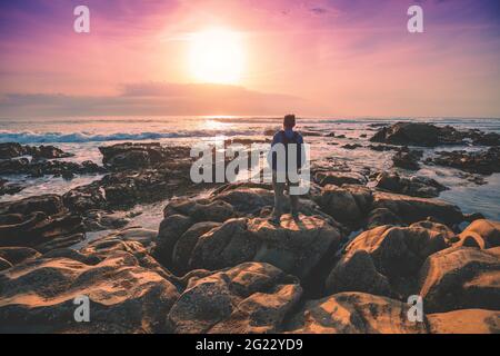 Paysage de mer en soirée. Rocky seashore à l'heure du coucher du soleil. Silhouette d'un touriste regardant un coucher de soleil magique sur la plage. Porto, Portugal Banque D'Images