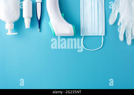 Gants médicaux, désinfectant, thermomètre, désinfectant pour les mains et masque chirurgical sur fond bleu Banque D'Images