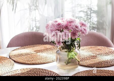 Un bouquet de chrysanthèmes gris est placé sur la table dans un vase en verre gris sur fond clair Banque D'Images