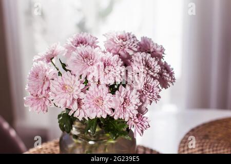 Un bouquet de chrysanthèmes gris est placé sur la table dans un vase en verre gris sur fond clair Banque D'Images