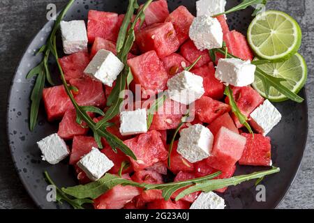 Salade de pastèques avec mozzarella, feta, arugula, vue en hauteur. Bol repas de légumes frais et savoureux sur table. Nourriture exotique verte saine Banque D'Images