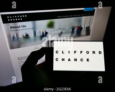 Personne tenant un smartphone avec le logo du cabinet d'avocats britannique Clifford chance LLP à l'écran devant le site Web. Mise au point sur l'affichage du téléphone. Banque D'Images