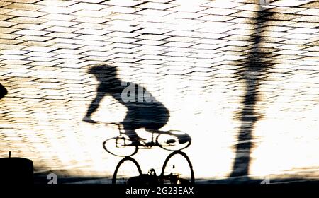 Silhouette d'ombre floue de personne à vélo sur le trottoir de la rue de la ville , par un jour ensoleillé Banque D'Images