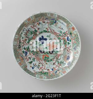 Soucoupe-plat avec animaux (mythologiques), paysages et sprays de fleurs. Plat de porcelaine à paroi ronde, peint en bleu sous-glaçure et sur le bleu, rouge, vert, jaune, aubergine, noir et or. Sur l'appartement un médaillon avec deux branches d'oiseaux et de fleurs; entrer dans le médaillon quatre compartiments avec un Feng Huang, un paysage avec une figure dans un bateau, un Qilin et des symboles chanceux, entre quatre petits compartiments avec des plantes à fleurs; Entre les champs de branches de fleurs et de papillons contre un sol vert tacheté noir; le bord avec des boissons de fleurs stylisées dans un entremêlé de cartouche Banque D'Images