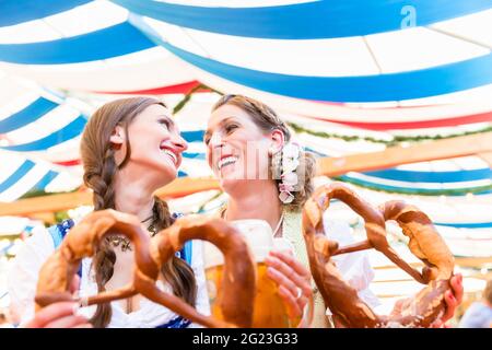 Deux amis portant dirndl sont debout dans une tente à bière Oktoberfest ou Dult avec bretzels géants Banque D'Images