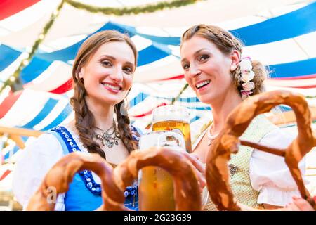 Deux amis portant dirndl sont debout dans une tente à bière Oktoberfest ou Dult avec bretzels géants Banque D'Images