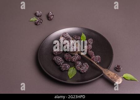 Mûres sur une plaque de céramique. Fruits congelés pour une alimentation saine. Concept minimaliste, fond en béton de pierre noire, pose plate Banque D'Images