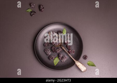 Mûres sur une plaque de céramique. Fruits congelés pour une alimentation saine. Concept minimaliste, fond en béton de pierre noire, vue de dessus Banque D'Images