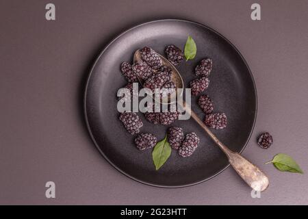 Mûres sur une plaque de céramique. Fruits congelés pour une alimentation saine. Concept minimaliste, fond en béton de pierre noire, vue de dessus Banque D'Images