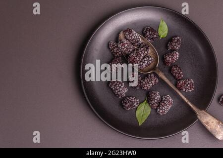 Mûres sur une plaque de céramique. Fruits congelés pour une alimentation saine. Concept minimaliste, fond en béton de pierre noire, vue de dessus Banque D'Images