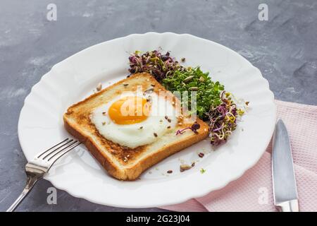 Un sandwich avec des œufs dans le trou du pain, des micro-légumes, des aliments sains petit déjeuner, fond gris Banque D'Images