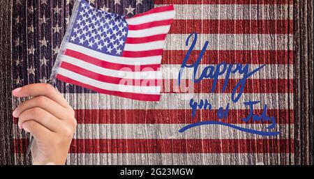 Joyeux texte du jour de l'indépendance et main tenant un drapeau américain contre nous drapeau sur fond de bois Banque D'Images