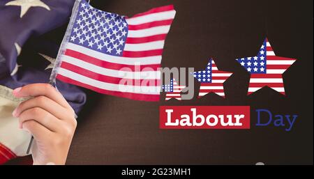 Joyeux texte de la fête du travail et main tenant un drapeau américain contre nous drapeau sur fond de bois Banque D'Images