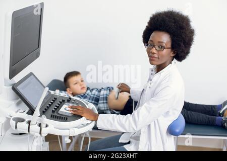 Pédiatrie et examen médical régulier. Une femme afro-américaine effectue une échographie des organes abdominaux d'un garçon patient à l'aide d'un équipement médical moderne dans une clinique Banque D'Images