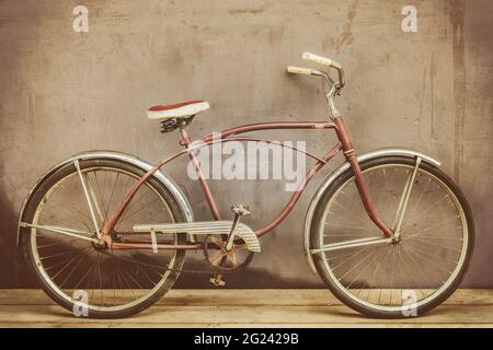 Vélo de croisière rouillé d'époque sur un plancher en bois avec un mur d'arrière-plan abîmé Banque D'Images