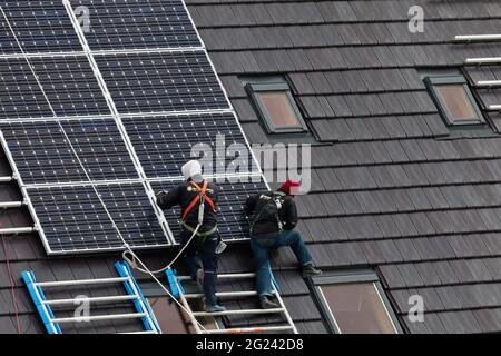 Ouvriers de la construction installant des panneaux solaires sur les toits de maisons nouvellement construites Banque D'Images