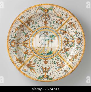 Plat avec Pomona. Plat rond de majolique peinte multicolore. Au milieu se trouve un cercle peint dans lequel une femme debout (Pomona) sur un sol avec un panier de fleurs dans sa main gauche (?). Le bord est divisé en quatre cours par quatre lignes à l'intérieur desquelles les dépliants fins et les animaux sont peints (patanazzi décor). Banque D'Images