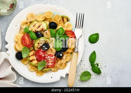 Pâtes salade fiocchi aux légumes courgettes grillées, tomates cerises, olives, basilic et parmesan dans une assiette blanche sur ardoise légère, pierre ou bétons Banque D'Images