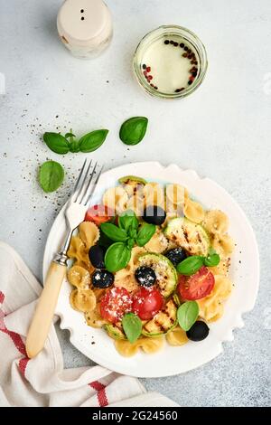 Pâtes salade fiocchi aux légumes courgettes grillées, tomates cerises, olives, basilic et parmesan dans une assiette blanche sur ardoise légère, pierre ou bétons Banque D'Images