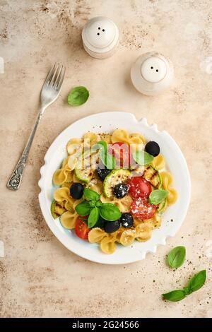 Pâtes salade fiocchi aux légumes courgettes grillées, tomates cerises, olives, basilic et parmesan dans une assiette blanche sur ardoise légère, pierre ou bétons Banque D'Images