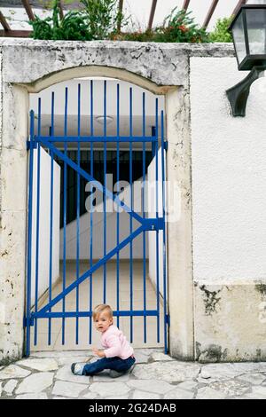 Une petite fille est assise devant une grille métallique près de la maison Banque D'Images