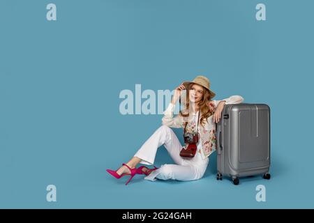 Bonne femme dans un chemisier et un pantalon assis près d'une valise Banque D'Images