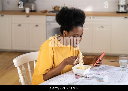 Une femme occupée tient son téléphone pour déjeuner sur le lieu de travail. Une femme architecte à plusieurs tâches peut manger rapidement Banque D'Images