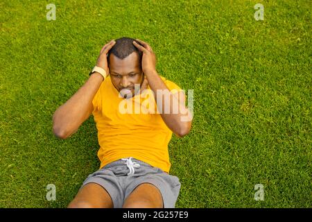 Jeune sportif concentré Afro américain mâle couché sur l'herbe verte faisant l'entraînement matinal à l'extérieur, positif sain entraînement noir gars actif entraînement abs entraînement Banque D'Images