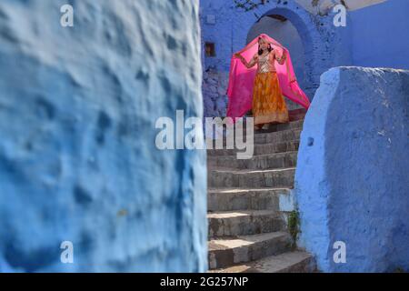 Femme en vêtements traditionnels marchant dans les escaliers, Chefchaouen, Maroc Banque D'Images