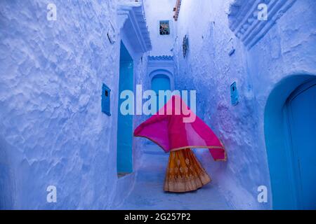 Vue arrière d'une femme marchant le long de la rue de la ville, Chefchaouen, Maroc Banque D'Images