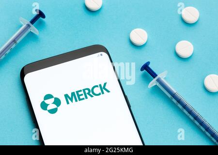 Galice, Espagne; 8 juin 2020 : téléphone intelligent affichant le logo Merck à l'écran et les pilules et la seringue sur fond bleu Banque D'Images