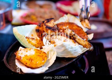 zoom dans la prise de coupe de pommes de terre trempée dans la sauce placée sur les feuilles de chou pour faire un épicé indien sizzler avec des légumes, des potatos, de la viande placée sur un Banque D'Images