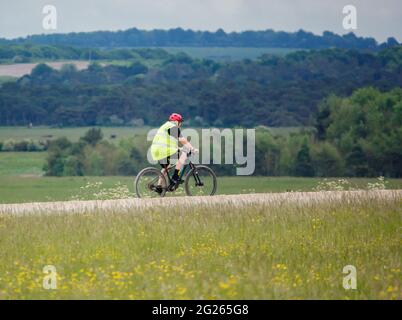 Cycliste portant une veste haute visibilité sur un vélo à pédales, il traverse une piste de pierre sur l'aire d'entraînement militaire de Salisbury Plain Banque D'Images