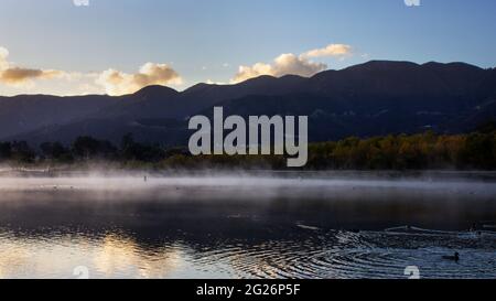 La brume plane sur la surface du lac avec des montagnes en arrière-plan. Banque D'Images