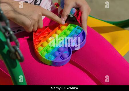 Une jeune fille tient un nouveau jouet pop en arc-en-ciel populaire dans ses mains. Un jouet anti-stress moderne pour le développement. Gros plan. Banque D'Images