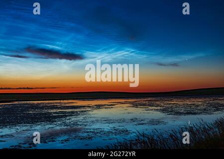 Des nuages lumineux et nocturnes dans le ciel de l'aube au-dessus d'un étang de prairie dans le sud de l'Alberta, au Canada. Banque D'Images