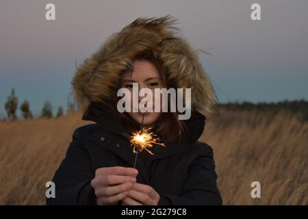 Fille dans une parka avec Sparkler pendant l'heure d'or Banque D'Images