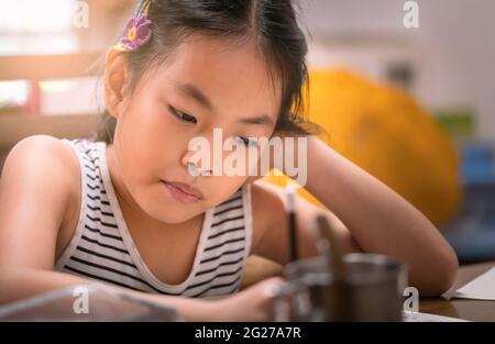 Portrait de l'asiatique belle fille d'enfant étudiant à la maison, gros plan de la fille assis à la table. Porte-crayons pour enfants, faites attention à l'écriture. Le c Banque D'Images