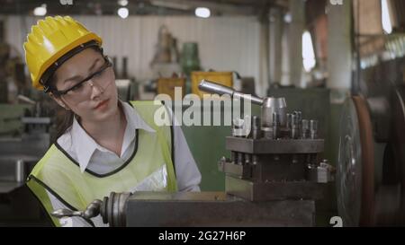 Ingénieur mécanique professionnel asiatique ou femme d'opération portant des lunettes de protection uniformes sécurité travail sur atelier métal tour industriel fait Banque D'Images