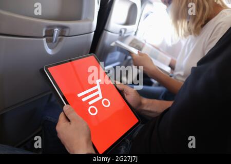 Homme tient une tablette fait des achats en ligne tout en étant assis dans la cabine de l'avion Banque D'Images