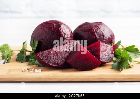 Betteraves bouillies entières et coupées sur une planche à découper avec des feuilles de persil sur fond blanc. Espace de copie, Banque D'Images