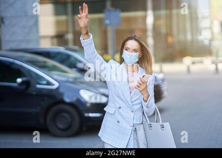 Femme d'affaires au masque prenant un taxi dans la ville Banque D'Images