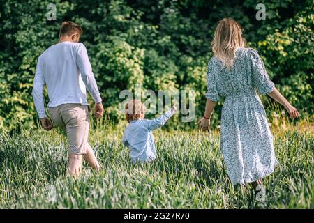 Famille tenant les mains avec l'enfant, vue arrière, mère, Père marchant à l'extérieur, deux parents sont dans le champ agricole, photo Banque D'Images