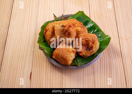 Pomme de terre Bonda, collation épicée indienne disposée dans une plaque d'acier bordée de feuilles de banane de manière traditionnelle, isolée sur fond texturé en bois. Banque D'Images