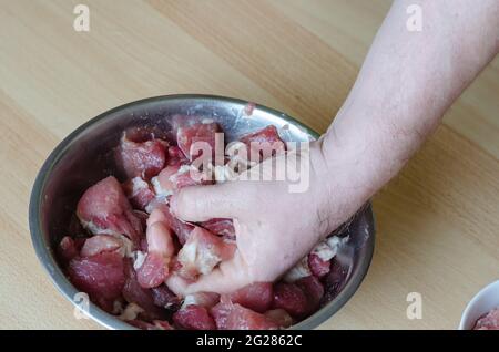 Préparation étape par étape de jambon haché fait maison. Étape 7 : une main mélange la viande hachée et les morceaux de viande dans un bol. Recette de cuisine. Banque D'Images