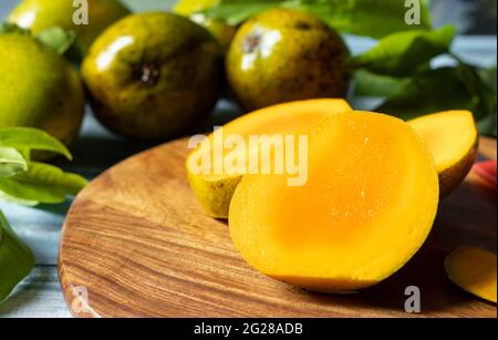 Concentrez-vous sur les tranches de mangue mûre sur une planche à découper en bois, ainsi que sur les mangues et les feuilles sur une table en bois Banque D'Images