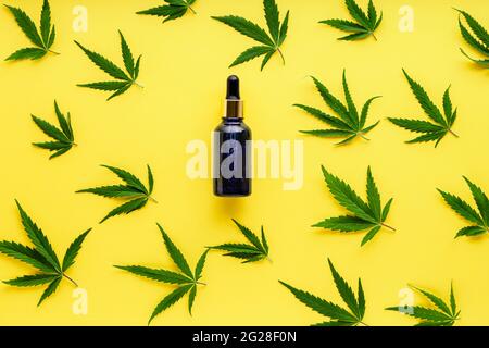 Sérum d'huile de chanvre dans un compte-gouttes en verre bleu avec des feuilles de cannabis. Motif feuilles de cannabis avec produit cosmétique huile de CBD sur fond jaune avec espace de copie Banque D'Images
