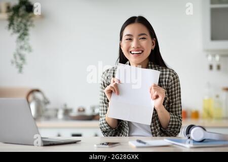 Femme asiatique joyeuse montrant du papier vide, intérieur de cuisine Banque D'Images